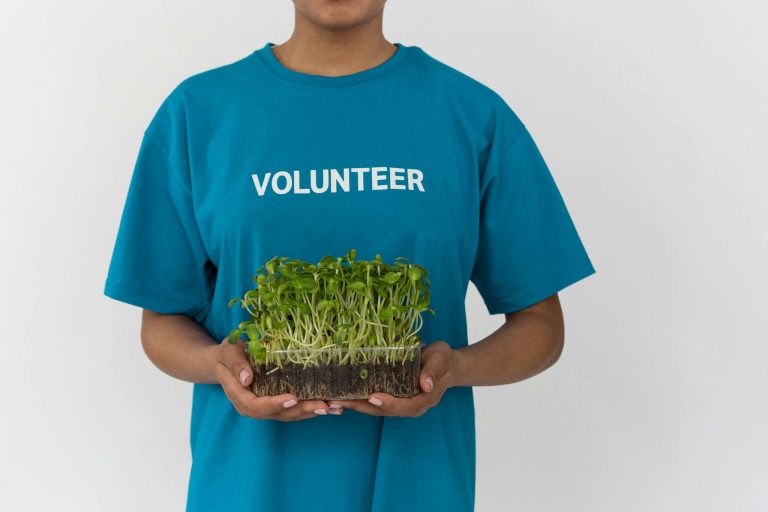 A volunteer in a blue T-shirt holding a tray of seedlings, advocating community and conservation efforts.